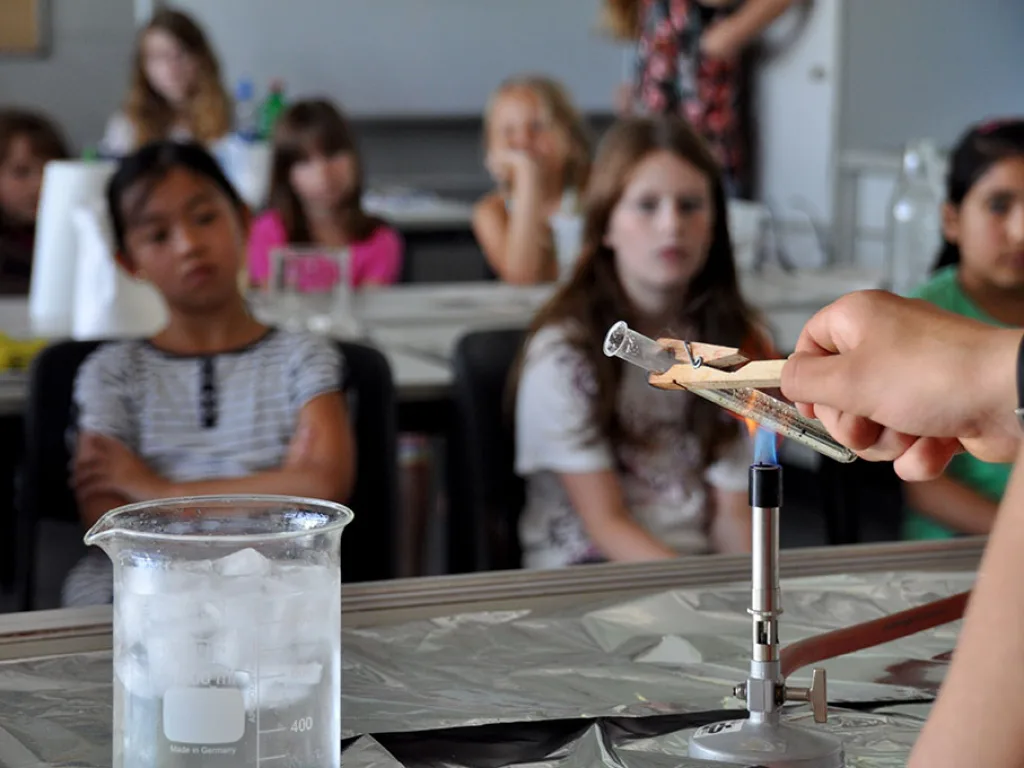Kinder beobachten ein Experiment mit einem Becherglas voller Nebel.